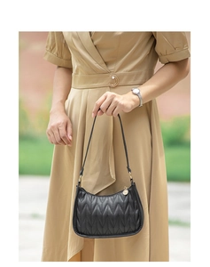 Detail of black quilted shoulder bag featuring V-shaped stitching and gold ring hardware