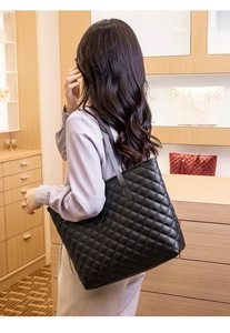 Rear view of a model wearing a black quilted tote bag with large capacity in a showroom