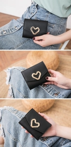 Detalle de una mini cartera de cuero negro con hebilla de corazón y diseño de sobre