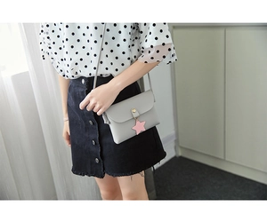 Close-up of a grey crossbody bag with a pink star pendant and gold clasp worn by a model