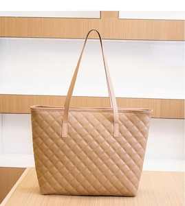 Detail of khaki quilted tote bag with diamond stitching and slim straps on wood