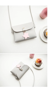 Detail of light gray square bag with pink star charm and round buckle on white desk