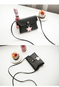 Detail of black mini crossbody bag featuring a pink star charm and gold snap button closure