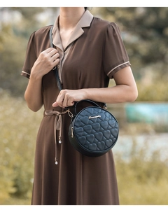 Detail of black round crossbody bag with heart quilting and golden hardware detail