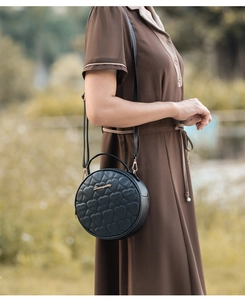 Detail of black round leather bag with heart quilting and gold logo for women