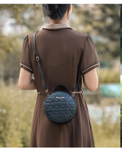 Outdoor street view of a woman wearing a black heart-quilted round crossbody bag