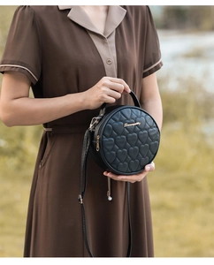 Close-up of black round bag featuring heart quilting and gold metal logo detail