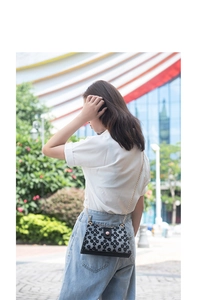 Détail d'un sac bandoulière vintage noir à fleurs avec chaîne dorée et bouton rose