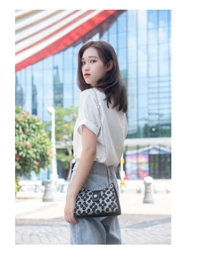 Sac bandoulière à fleurs avec chaîne dorée porté par un mannequin devant un mur de verre