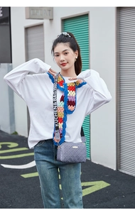 Detail of printed crossbody bag with wide lettered strap and colorful crochet scarf