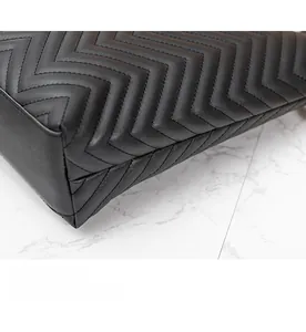 Détail des coutures du cuir noir matelassé et de la texture à motif en V d'un grand sac cabas