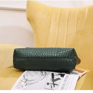 Detalle de bolso tote de cuero trenzado verde con textura fina sobre un sofá
