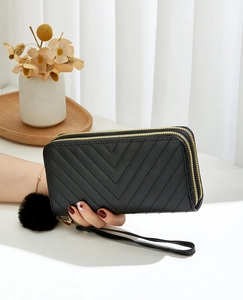 Close-up of black long clutch bag with V-quilt pattern, double zippers and fur pompom