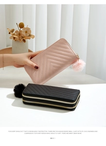 Close-up of long quilted wallets in pink and black with pompom charms and gold zippers