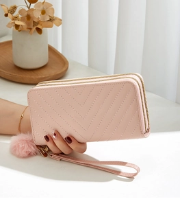 Detail of pink double zipper clutch bag with V-shaped quilting and a soft fur pompom