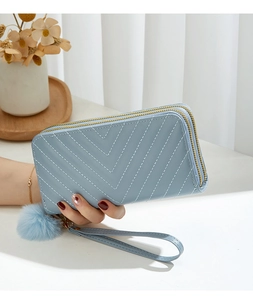 Close-up of light blue long double zipper wallet with V-shaped stitching and plush ball charm