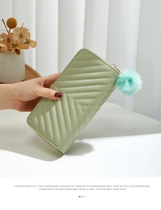 Detail of long quilted wallet in sage green featuring a soft pompom and twill texture