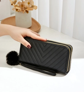 Macro view of black long wallet with V-quilted pattern, double zippers, and fur ball charm