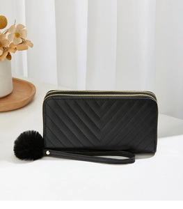 Detail of black double zipper long wallet with chevron quilting and faux fur pom pom charm