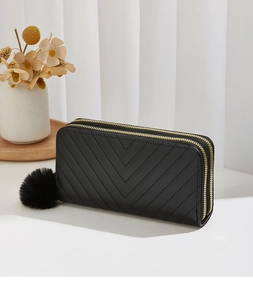 Detail of black V-quilted long wallet with double zippers and fur ball charm on tray
