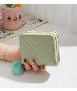 Close-up of mint green quilted double zipper wallet with soft faux fur pompom charms