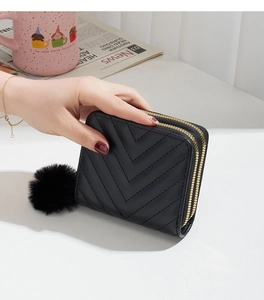 Detail of black quilted leather wallet with double zippers and soft pompom pendant