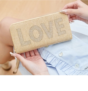 Close-up of beige straw woven clutch with LOVE rhinestone lettering and wristlet strap