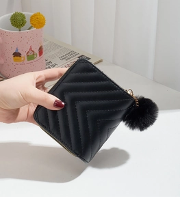 Detail of black quilted double zipper wallet with stylish pompom pendant