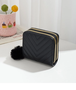 Detail of black V-quilted faux leather wallet with gold zippers and pompom charm