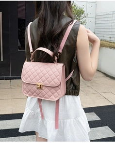 Pink quilted backpack with golden twist lock shown on a model in an outdoor street setting