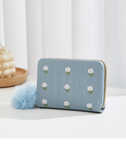 Detail of light blue PU leather mini purse featuring floral embroidery and plush ball