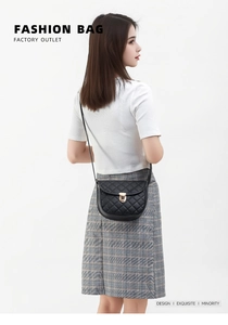 Détail d'un sac bandoulière noir matelassé avec un fermoir rotatif doré en forme de U