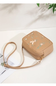 Detail of floral leaf embroidery and 3D butterfly ornament on a mini beige crossbody bag