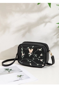 Detail of floral embroidery and 3D butterfly on a black leather crossbody camera bag