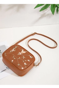 Detail of embroidered floral and butterfly patterns on a brown square crossbody bag