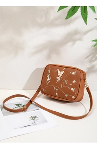 Detailed close-up of plant flower embroidery and 3D butterfly on brown crossbody bag