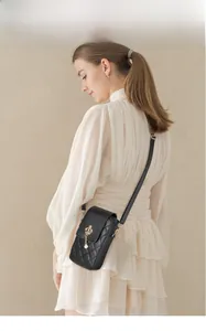 Close-up of black quilted phone bag with gold crown and pearl charm on model