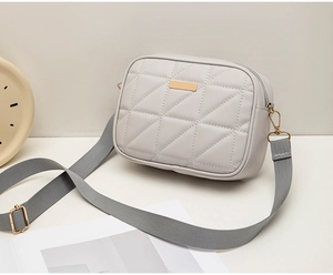 Detail of light grey quilted crossbody bag with golden hardware and woven strap