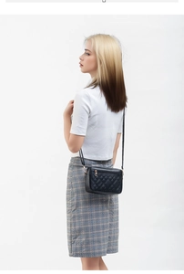 Detailed close-up of a black quilted crossbody bag with gold-tone metal zipper and strap