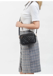 Close-up of a black quilted crossbody bag with gold hardware worn by a model