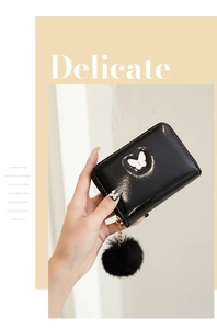 Détail d'un portefeuille en cuir verni noir avec ornement papillon et pompon décoratif
