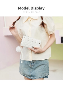 White quilted long wallet with golden studs and fur pom-pom charm held by a model