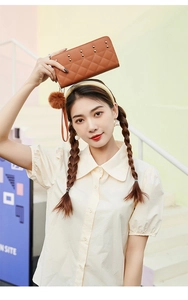 Detail of brown quilted leather purse featuring metallic studs and a soft pom-pom charm