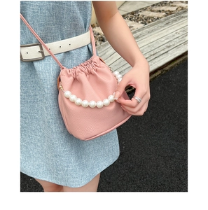 Detailed view of pink lychee leather bucket bag featuring a large pearl handle and drawstring