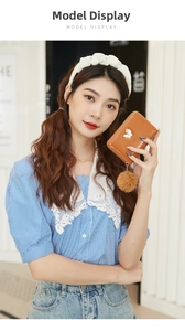 Mini portefeuille en cuir PU marron avec papillon et pompon tenu par un mannequin