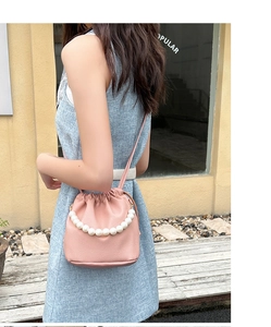 Close-up of pink drawstring bucket bag with a pearl handle worn as a crossbody purse