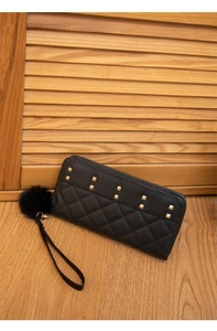Quilted black long wallet with gold studs and a fluffy pom-pom charm on a wood floor