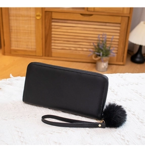 Detail of long black quilted wallet with faux fur pompom charm and wrist strap