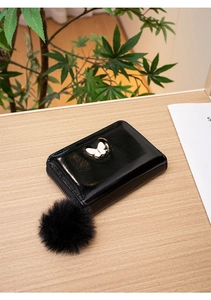 Détail du portefeuille en cuir PU noir brillant avec papillon en métal et pompon en peluche