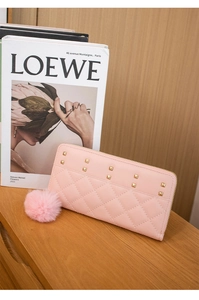Pink quilted long wallet with gold studs and pom-pom charm on a wooden table
